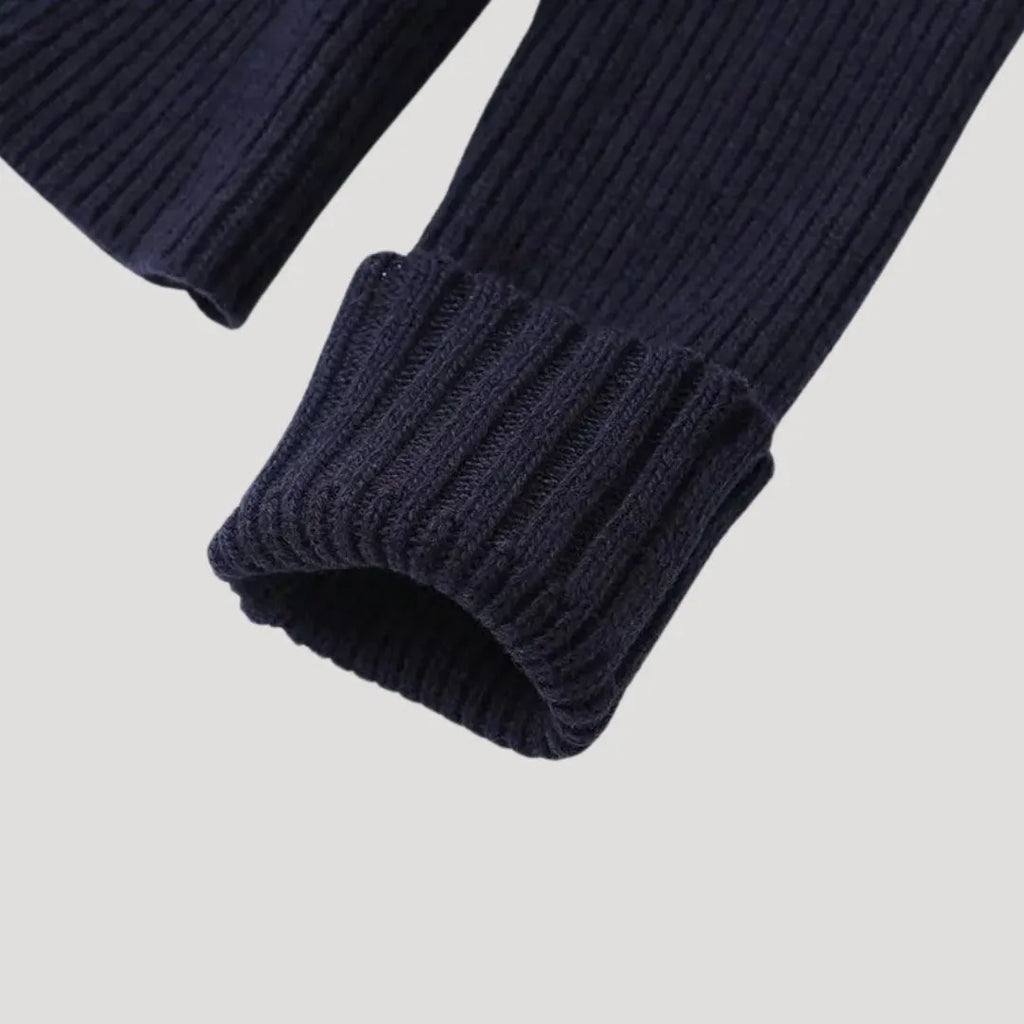 Close-up of a navy blue ribbed knit cardigan sleeve with a folded cuff.