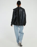 Blouson femme noir en similicuir, style motard, avec fermeture éclair et deux poches latérales.